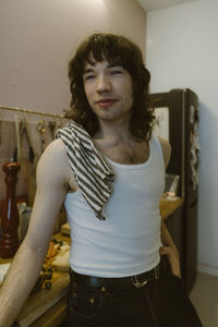 Smiling young man wearing undershirt standing with hand in pocket near kitchen counter at home