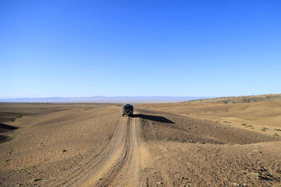 Rear view of man walking on sand at desert against clear blue sky