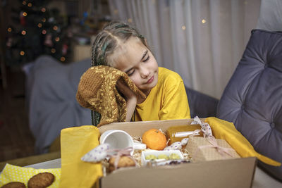 Girl packing care box with tea, honey, cookies and knitted wool socks for grandmother on christmas