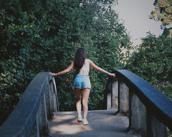 Rear view of young woman walking on footbridge against trees