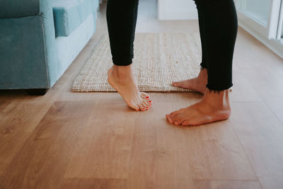 Barefoot legs of crop unrecognizable couple standing on wooden floor in cozy room at home barefoot