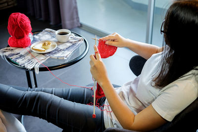 High angle view of woman knitting red wool while sitting at home