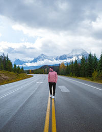 Rear view of man walking on road against sky