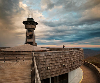 Lighthouse by building against sky during sunset