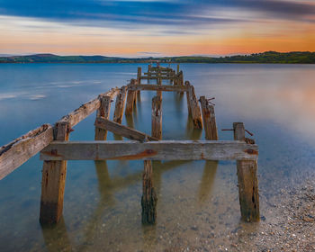 Wooden posts in lake against sky during sunset