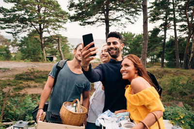 Happy male and female friends taking selfie from smart phone in forest