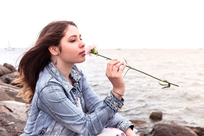 Young woman sitting on shore at beach against sky