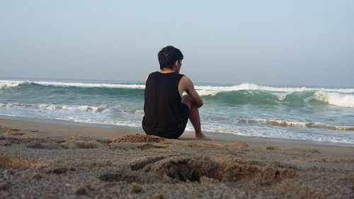 Full length of man sitting on beach against clear sky