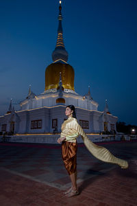 Full length of teenage girl in traditional clothing standing against temple at night