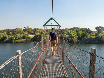 Rear view of man walking on footbridge over river zambezi, chinyingi, zambia