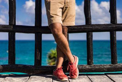 Low section of man standing on railing against sea