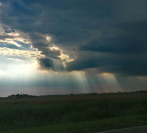 Sunlight streaming on field against dramatic sky