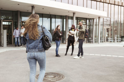 Rear view of woman walking towards friends at university campus