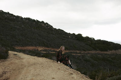 Teenage girl sitting on mountain against sky