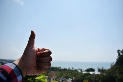 Close-up of hand showing thumbs up against clear sky