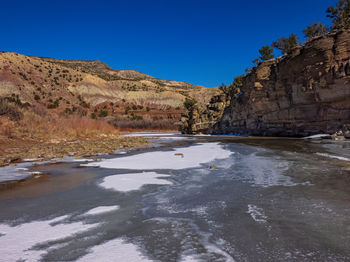 Scenic view of frozen river and desert landscape against clear blue sky