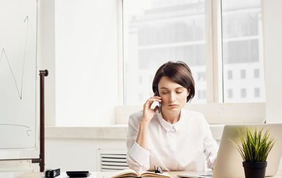 Young woman using mobile phone while sitting on table