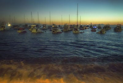 Boats moored in calm sea against dramatic sky