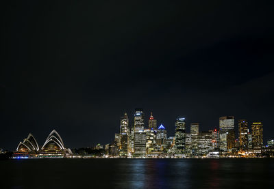 Illuminated city by buildings against sky at night