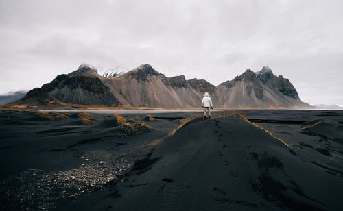 Rear view of man standing on land against mountains and sky