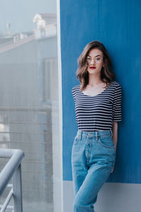 Portrait of beautiful young woman standing against blue wall
