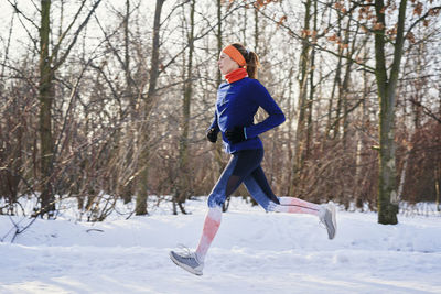 Woman running near bare trees during snow in winter