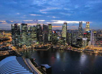 Illuminated city by river against sky