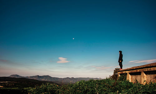 Man standing on retaining wall against sky