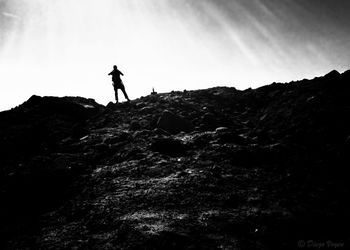 Silhouette man standing on rock against sky