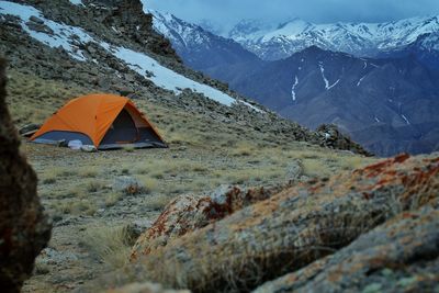 Orange color tent being set up in the mountains and valley in ladakh and a space for text.