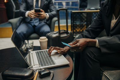 Midsection of businesswoman holding credit card using laptop at hotel lounge