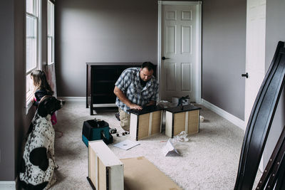 Father repairing drawers while daughter looking through window at home