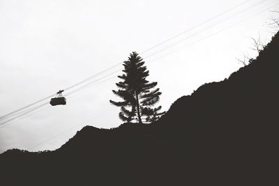 Low angle view of silhouette overhead cable car above mountain against sky