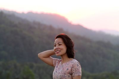 Smiling woman looking away against mountains during sunset