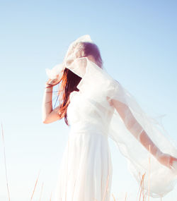 Low angle view of woman in white dress against clear sky on sunny day