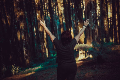 Rear view of woman with arms raised standing in forest