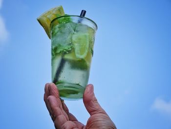 Midsection of person holding drink against blue sky