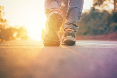 Low section of man walking on road during sunset