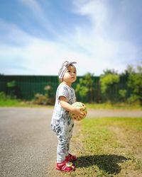 Full length of cute girl holding ball while standing on field
