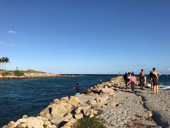 People on pier over sea against blue sky