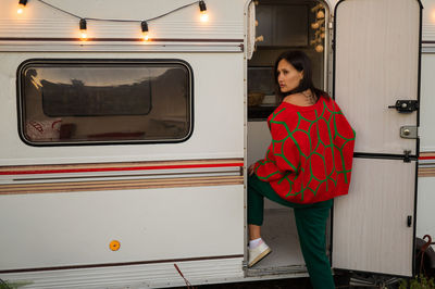 Caucasian woman in oversized red knitted jumper travels in motorhome in autumn