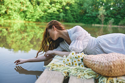 Side view of young woman sitting by lake