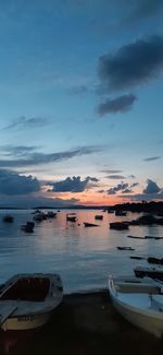 Boats moored in sea against sky at sunset