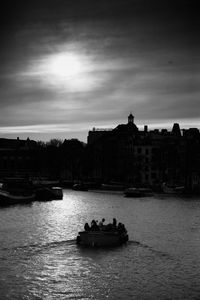 People on boat in river against sky in city