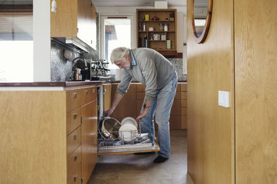 Senior man putting plates in dishwasher at kitchen