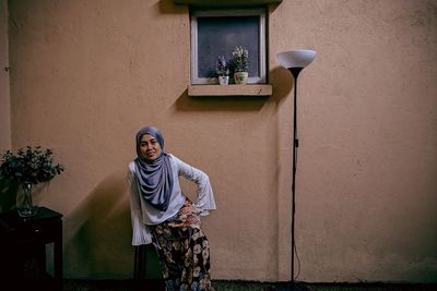 Portrait of woman wearing hijab while sitting against wall