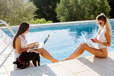 Beautiful women using laptop while sitting by swimming pool