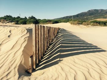 Shadow of wooden fence on sandy beach during sunny day