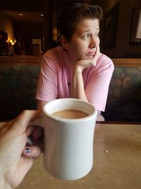 Cropped holding coffee cup against woman sitting at table in restaurant