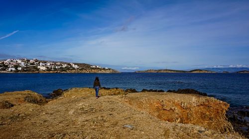 Rear view of man standing at beach against blue sky
